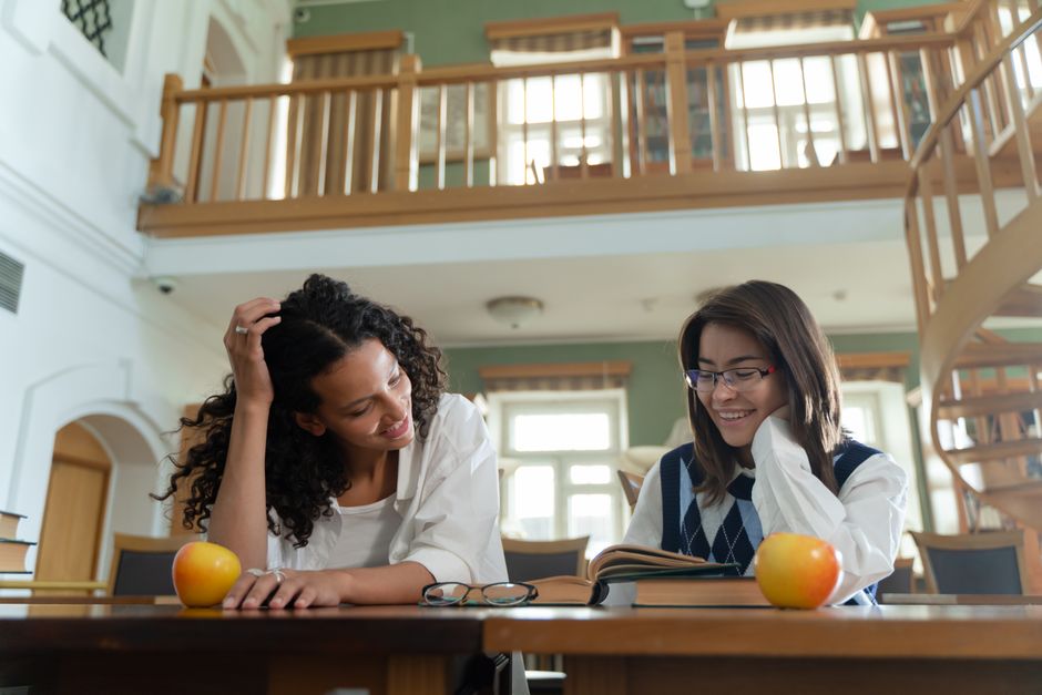 Two students studying together with an open book at a bright library table